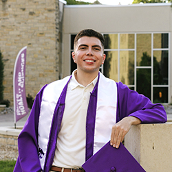 Javier Vazquez standing in graduation gown outside Justin Hall
